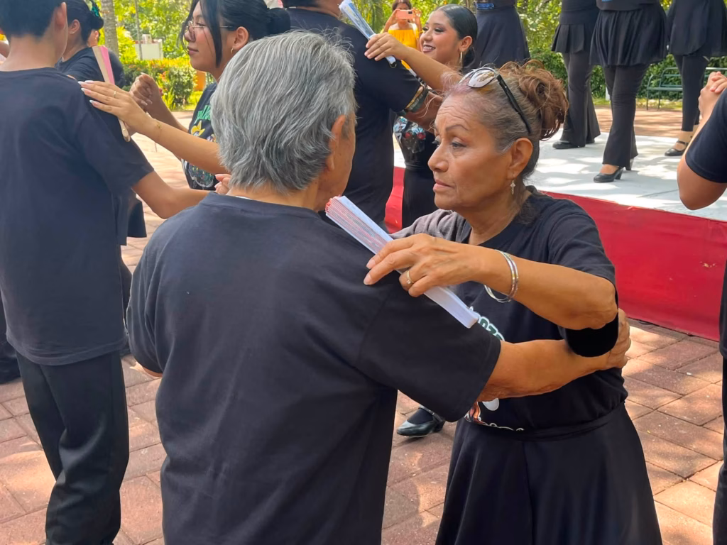 ¿Qué Hacer El Día De Los Abuelos En Tabasco? 75 Una Mujer Mayor Abrazando Cariñosamente A Otra Persona Durante Una Actividad De Baile Al Aire Libre En El Centro Cultural Quinta Grijalva, Rodeada De Otros Asistentes Vestidos Con Ropa Negra En Un Espacio Arbolado.