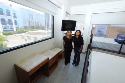 Dos Estudiantes Universitarias Posan En El Interior De Una Habitación Amueblada De La Villa Universitaria En Villahermosa, Con Literas, Muebles De Madera Y Una Gran Ventana Con Vista Al Exterior.