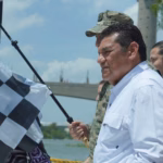 El Gobernador Javier May Rodríguez Sosteniendo Una Bandera A Cuadros En El Muelle De Villahermosa Para Dar El Banderazo De Salida A La Carrera Motonáutica.