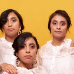 Las Cinco Hermanas Aguilar Paz, Conocidas Como Las Quintillizas De Villahermosa, Posando Juntas En Una Sesión Fotográfica Grupal Con Blusas Blancas De Encaje Sobre Un Fondo Amarillo Y Superficie Coral.