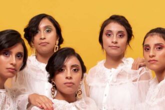 Las Cinco Hermanas Aguilar Paz, Conocidas Como Las Quintillizas De Villahermosa, Posando Juntas En Una Sesión Fotográfica Grupal Con Blusas Blancas De Encaje Sobre Un Fondo Amarillo Y Superficie Coral.