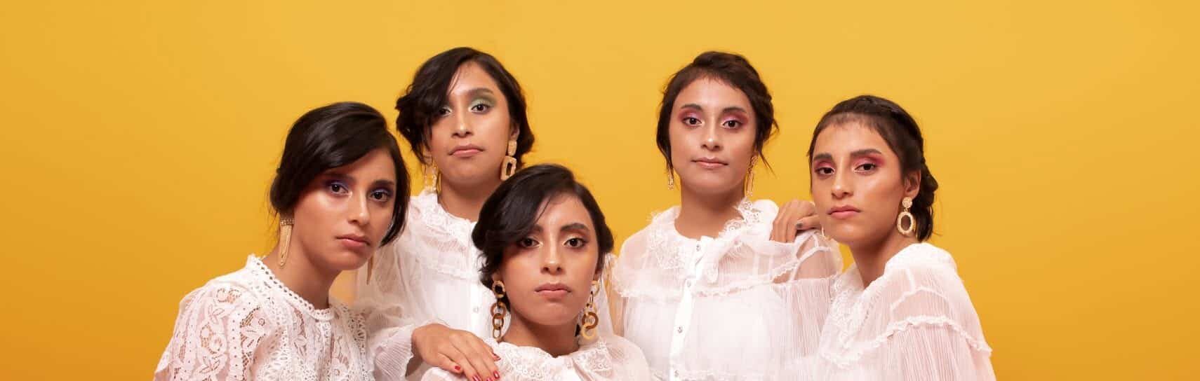 Las Cinco Hermanas Aguilar Paz, Conocidas Como Las Quintillizas De Villahermosa, Posando Juntas En Una Sesión Fotográfica Grupal Con Blusas Blancas De Encaje Sobre Un Fondo Amarillo Y Superficie Coral.