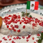 Chile En Nogada Tradicional Servido Sobre Un Plato Decorado, Cubierto Con Crema De Nuez De Castilla, Granos De Granada Roja, Perejil Y Una Pequeña Bandera De México.