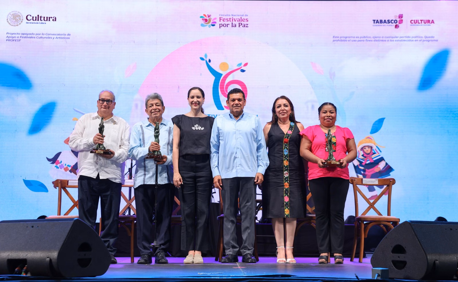 Seis Personas De Pie Sobre Un Escenario En Una Ceremonia De Entrega De Premios Del Circuito Nacional De Festivales Por La Paz. El Grupo Está Posando Para Una Fotografía, Y Las Tres Personas De Los Extremos Sostienen Estatuillas De Premios. El Fondo Muestra Una Gran Pantalla Led Con El Logotipo Del Festival Y Texto En Español.