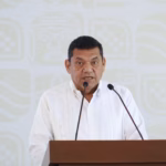El Gobernador De Tabasco, Javier May Rodríguez, Vistiendo Una Guayabera Blanca, Al Frente De Un Pódium De Madera Con Micrófonos Durante La Conferencia De Prensa Matutina.