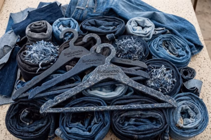Tres Perchas De Ropa Sostenibles, De Color Azul Con Motas Blancas Y Grabadas Con La Inscripción &Quot;Biogancho - Hecho En Tabasco - Reciclado&Quot;, Están Dispuestas En Primer Plano Sobre Una Colección De Vaqueros Enrollados Y Restos De Tela Vaquera Deshilachada Sobre Una Superficie Jaspeada.