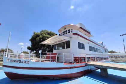 Una Toma De Ángulo Bajo De La Histórica Embarcación &Quot;Mensajero De La Salud&Quot; En Exhibición, Pintada De Blanco Y Rojo Sobre Una Superficie Azul Simulando Agua, Con Un Muelle De Concreto Que Conduce A Ella Bajo Un Cielo Despejado.