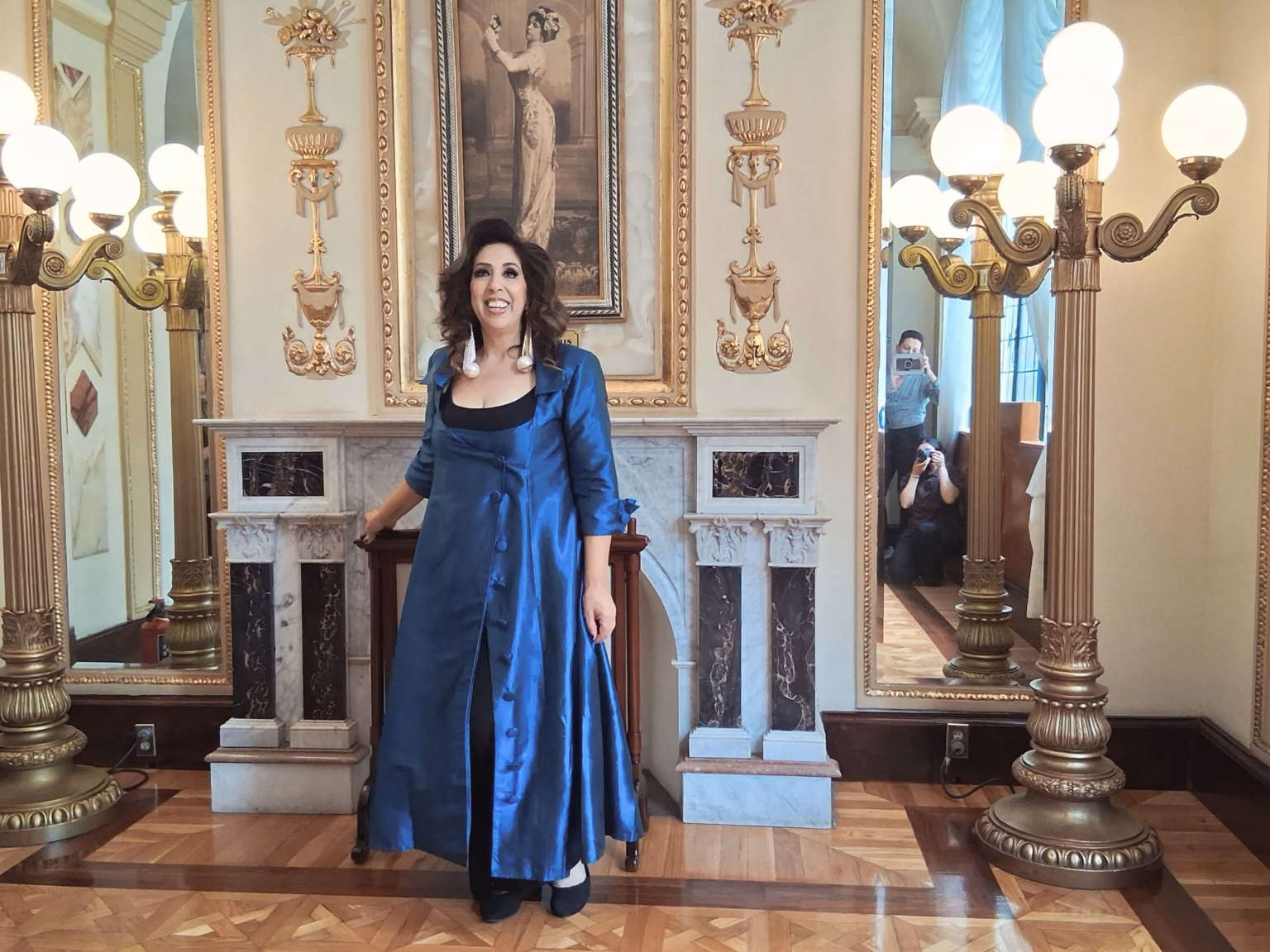 Regina Orozco Recuerda A La Tabasqueña Esperanza Iris Y Revela Historia De Aparecidos En Su Teatro 71 La Soprano Y Actriz Mexicana Regina Orozco Posa Sonriente Con Un Abrigo Largo De Satén Azul En El Histórico Foyer Del Teatro De La Ciudad Esperanza Iris, Luciendo Un Peinado Ondulado Frente A La Chimenea De Mármol Y Retratos De Época.