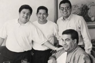 Fotografía En Blanco Y Negro Del Personal Y Fundadores En La Estancia Del Bife 25 Aniversario, Sonriendo Junto A Un Comensal En La Mesa Frente A Un Corte De Carne.