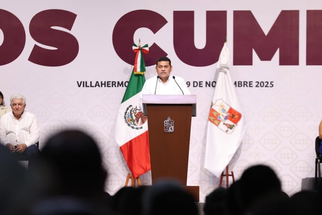 Conoce Cuándo Se Celebrará El Segundo Año De Resultados Y Avances Del Gobierno Del Pueblo Con Javier May El Gobernador Javier May Rodríguez Dirige Un Mensaje Desde Un Atril De Madera Con El Escudo De Tabasco, Flanqueado Por La Bandera De México Y La Bandera Estatal, Frente A Una Audiencia En Un Recinto Oficial.