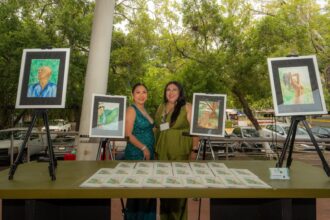Dos Mujeres Posan Sonrientes Junto A Una Mesa Llena De Folletos Y Caballetes Con Obras De Arte Durante La Exposición Cultural En Tabasco.