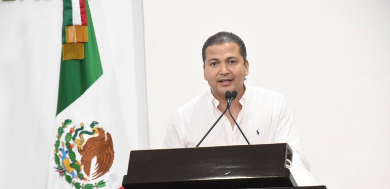 Jorge Orlando Bracamonte Hernández Emitiendo Un Discurso Desde La Tribuna, Luciendo Una Camisa Blanca Frente A La Bandera De México.