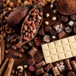Variedad De Chocolates Finos, Barras De Chocolate Blanco Y Oscuro, Frutos Secos, Rajas De Canela Y Una Mazorca De Cacao Abierta Con Sus Semillas Sobre Una Superficie De Madera.