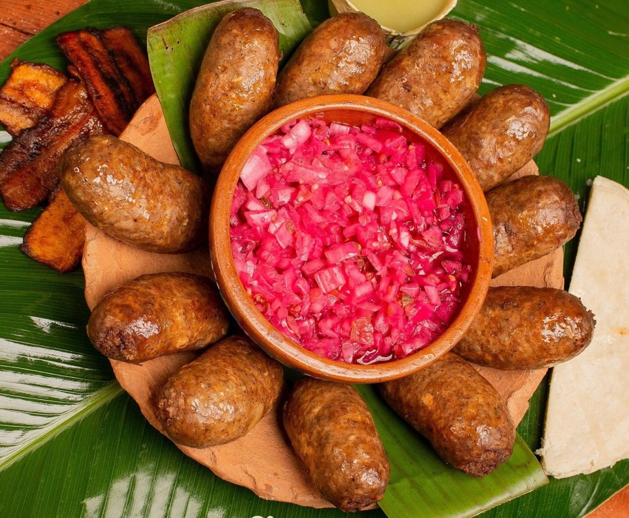 El Secreto Culinario De Jalpa: Tradición, Sabor E Identidad De La Butifarra Tabasqueña Plato De Barro Con Butifarras De Jalpa Dispuestas Alrededor De Un Recipiente Central Con Cebolla Morada Picada, Acompañado De Plátanos Fritos Y Tortillas Sobre Hojas De Plátano.