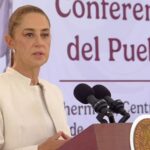 La Presidenta De México, Claudia Sheinbaum Pardo, Durante Una Conferencia De Prensa Desde Villahermosa, Tabasco, Vistiendo Un Saco Beige Y Hablando Frente A Micrófonos Y El Escudo Nacional.