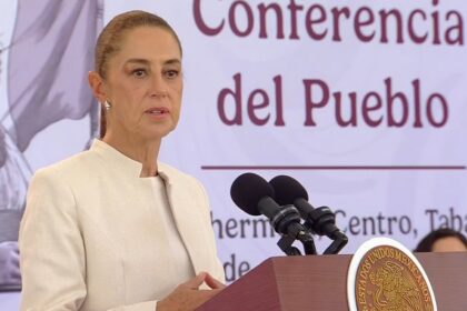 La Presidenta De México, Claudia Sheinbaum Pardo, Durante Una Conferencia De Prensa Desde Villahermosa, Tabasco, Vistiendo Un Saco Beige Y Hablando Frente A Micrófonos Y El Escudo Nacional.