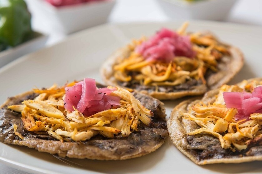 Primer Plano De Un Plato Blanco Con Tres Panuchos Tradicionales Servidos Con Base De Frijol, Carne Deshebrada Y Cebolla Morada Encurtida Encima.