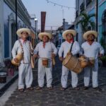 Cuatro Músicos Tradicionales De Tabasco Conocidos Como Tamborileros Portando Vestimenta Blanca, Sombreros Y Tambores En Una Calle Colonial.