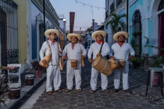 Cuatro Músicos Tradicionales De Tabasco Conocidos Como Tamborileros Portando Vestimenta Blanca, Sombreros Y Tambores En Una Calle Colonial.