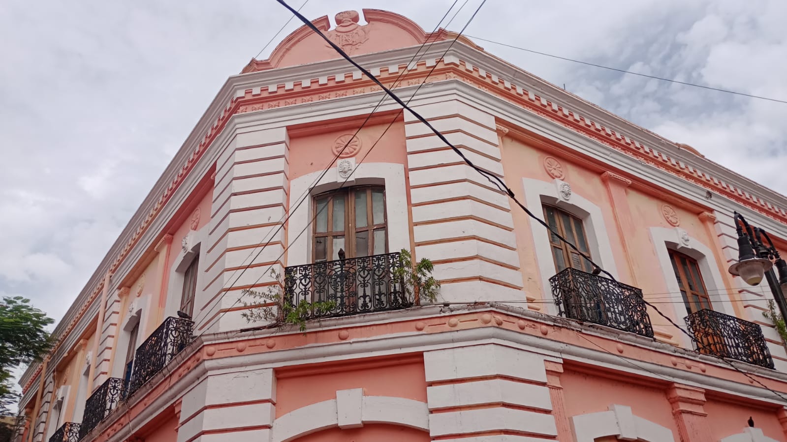 Memoria De Piedra Y Olvido: La Fascinante Historia Del Edificio Del Banco De México En Villahermosa Fachada De Un Edificio Histórico De Dos Pisos En Tonos Salmón Y Blanco Con Balcones De Herrería Negra, Ubicado En Una Esquina Del Centro Histórico De Villahermosa.