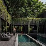 Diseño Arquitectónico De Casa Roca Con Fachada Monolítica En Color Negro Absoluto, Piscina Central Reflectante Y Vegetación Abundante.