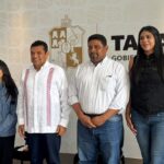 Una Toma De Plano Medio Muestra A Cuatro Personas Posando De Pie, Sonrientes, En El Centro De Un Escenario. El Fondo Es Una Pared Decorada Con Un Patrón De Relieves Sutiles Y En El Centro, El Escudo De Armas De Tabasco. A La Derecha, Parcialmente Visible, Está La Parte Superior De Un Letrero Con El Texto Grande &Quot;Tabasco&Quot; Y Debajo &Quot;Gobierno Del Pueblo&Quot;.