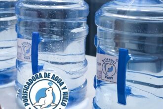 Garrafones Azules De Leonella Purificadora De Agua Alineados En Una Mesa Mientras Una Persona De Blusa Roja Se Acerca A Manipularlos