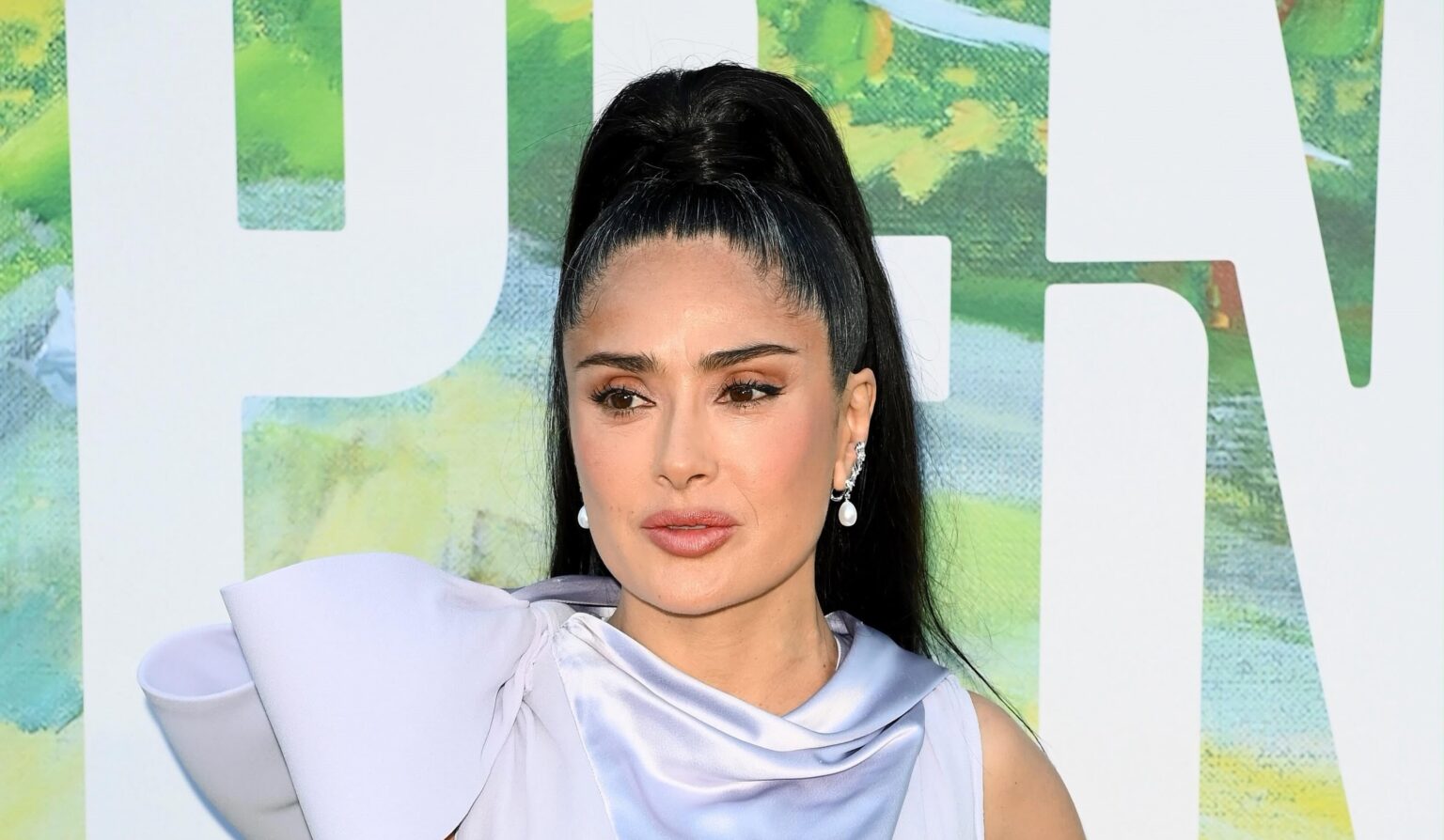 Salma Hayek Luciendo Un Vestido Satinado De Color Lavanda Con Un Lazo Estrucutrado En El Hombro Y Una Coleta Alta Tirante Durante Un Evento De Alfombra Roja.