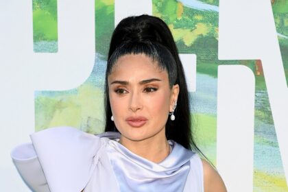 Salma Hayek Luciendo Un Vestido Satinado De Color Lavanda Con Un Lazo Estrucutrado En El Hombro Y Una Coleta Alta Tirante Durante Un Evento De Alfombra Roja.